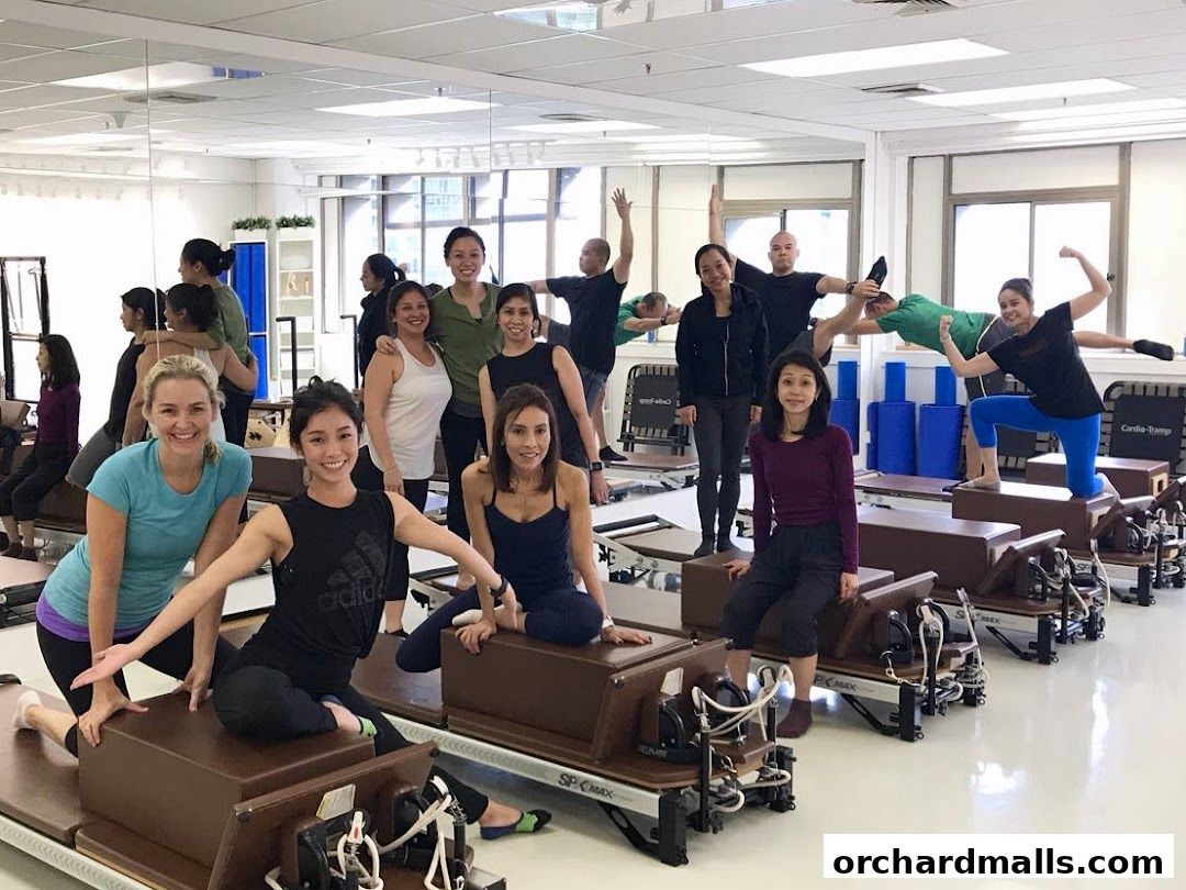 A group of people posing in a Pilates studio with reformers and equipment.