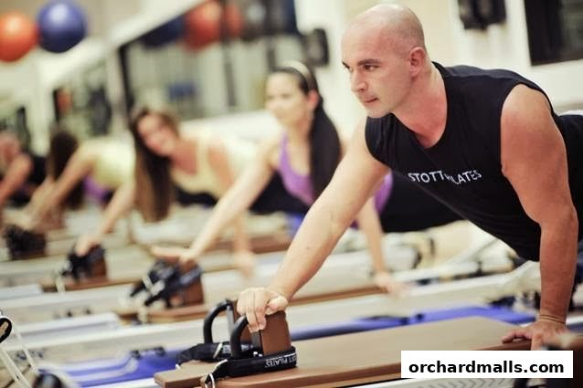 Instructor leads a Pilates class on reformers with participants in the background.
