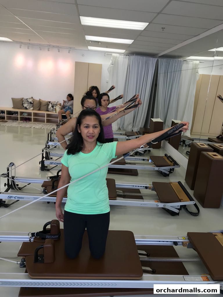 Women exercising on Pilates reformers in a bright studio with mirrors and equipment.