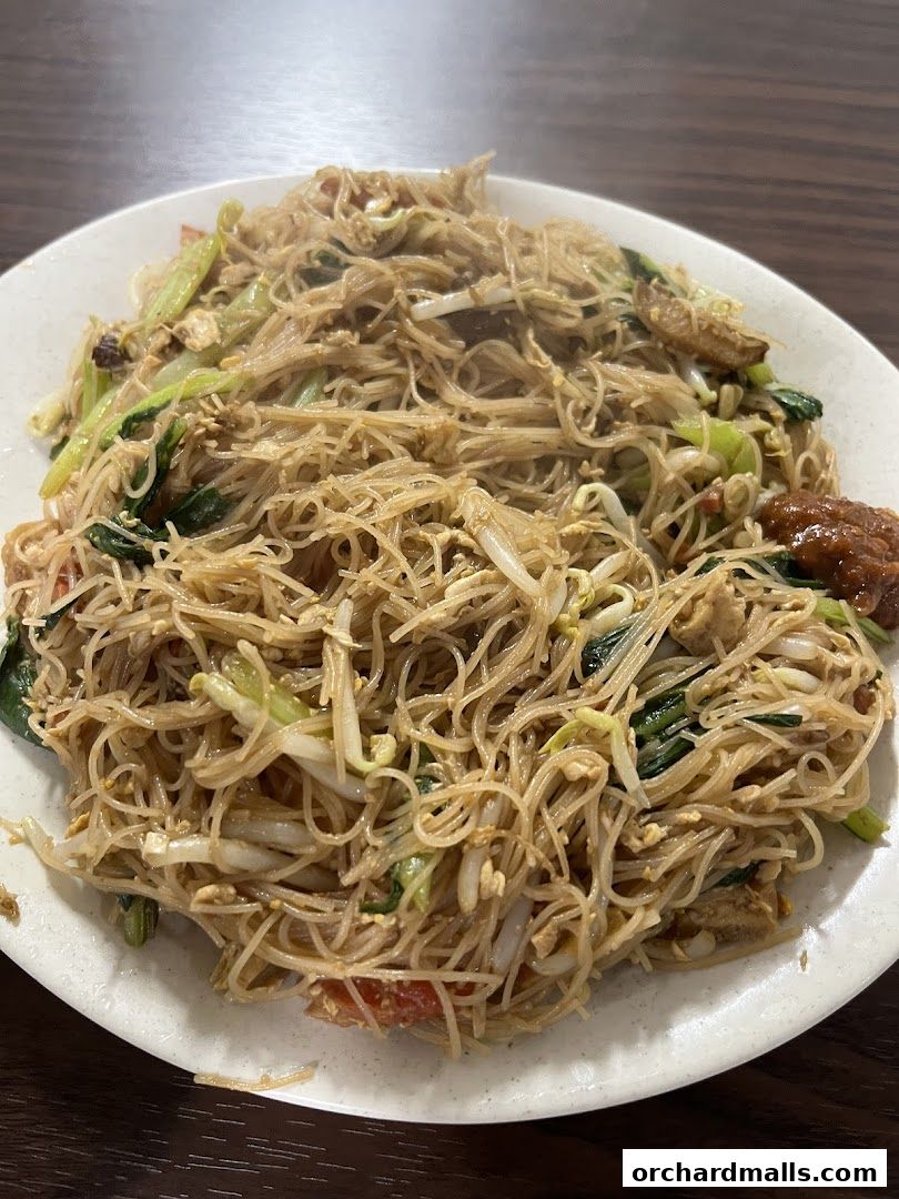 A close-up shot of a plate of stir-fried noodles with vegetables and a side of chili paste.