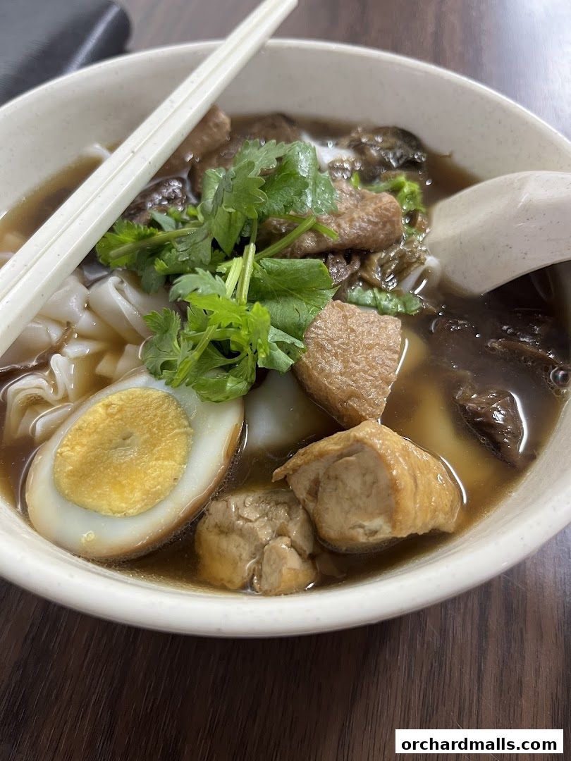 A close-up of a bowl of noodles with egg, tofu, and herbs.