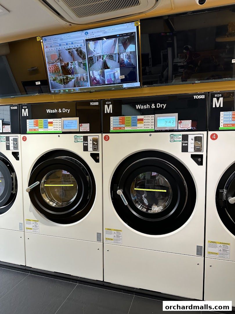 Row of modern washing and drying machines with digital displays and security monitors above.