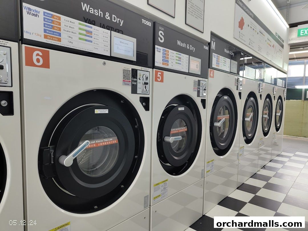 A row of commercial washing and drying machines with price lists displayed.