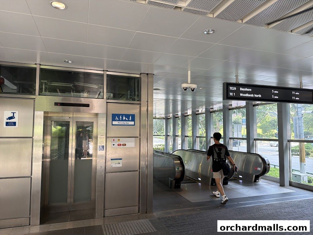 A person walks past escalators and an elevator at a transit station with digital signage.