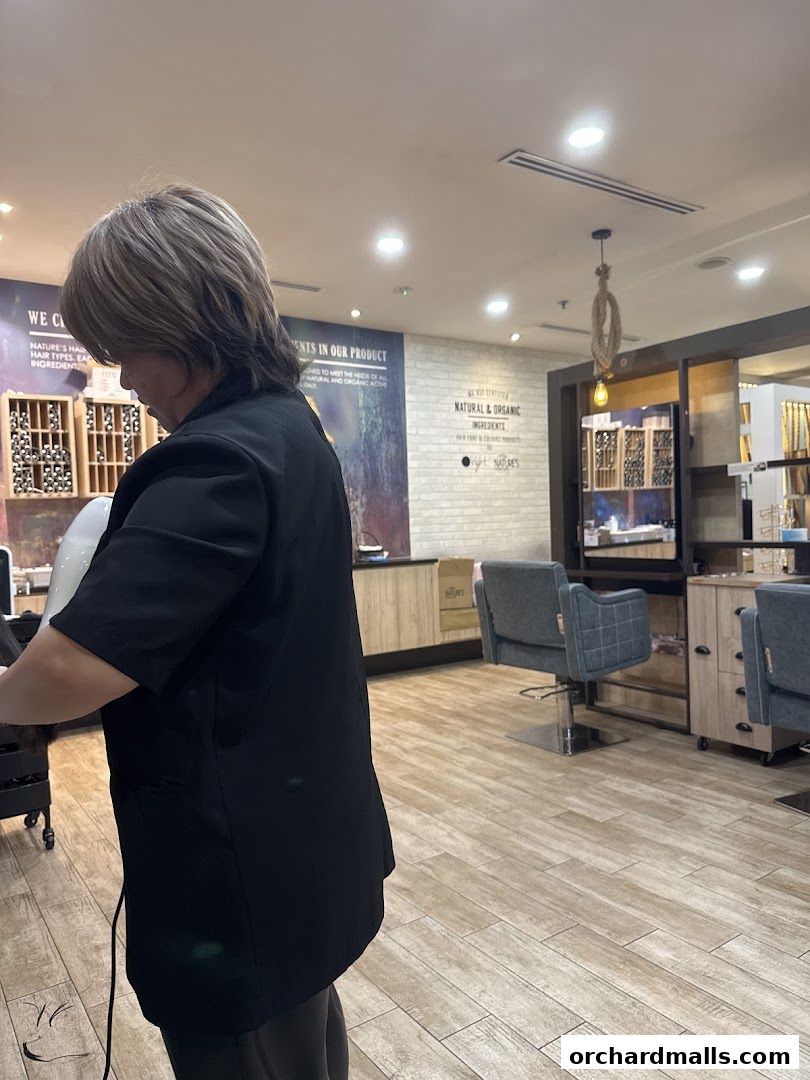 A stylist works on a client's hair in a salon with natural and organic product displays.