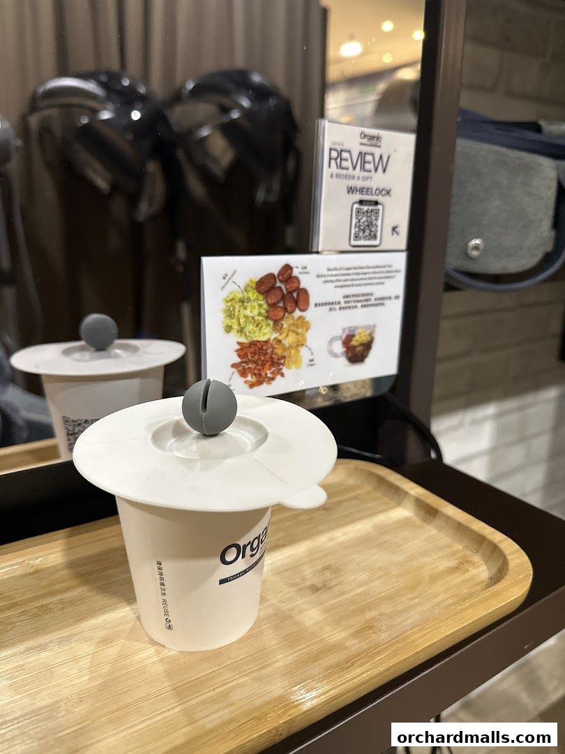 A cup with a lid on a wooden tray, with hair dryers and a sign in the background.