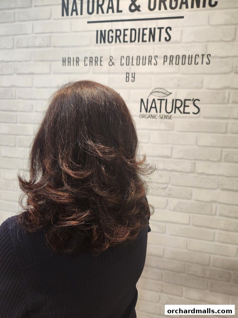 A person's back with styled brown hair in front of a brick wall with text.