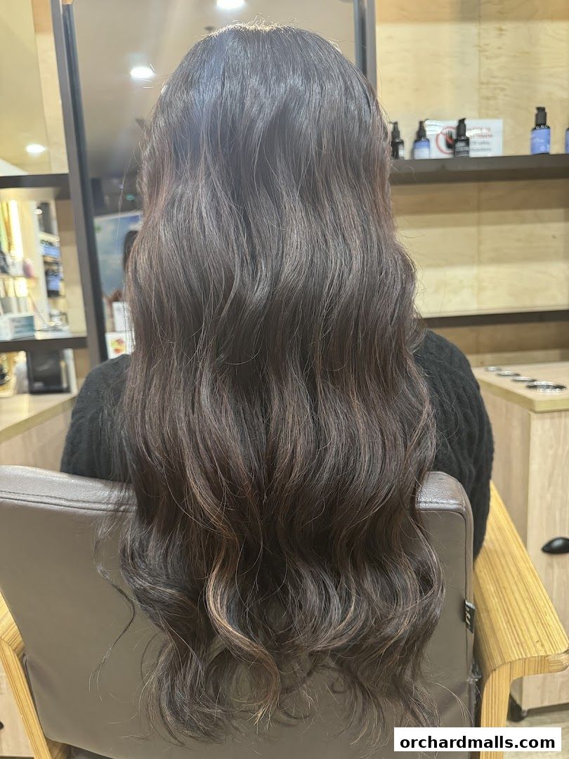 A person with long, wavy, dark brown hair sitting in a salon chair.
