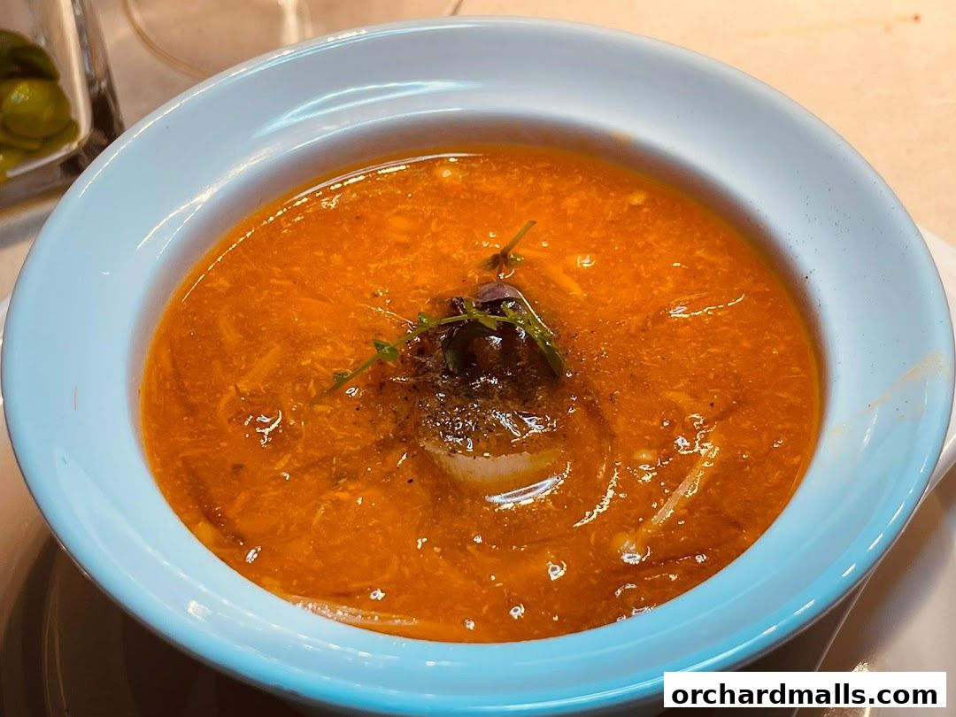 A close-up of a steaming bowl of rich, orange-colored soup with visible ingredients.