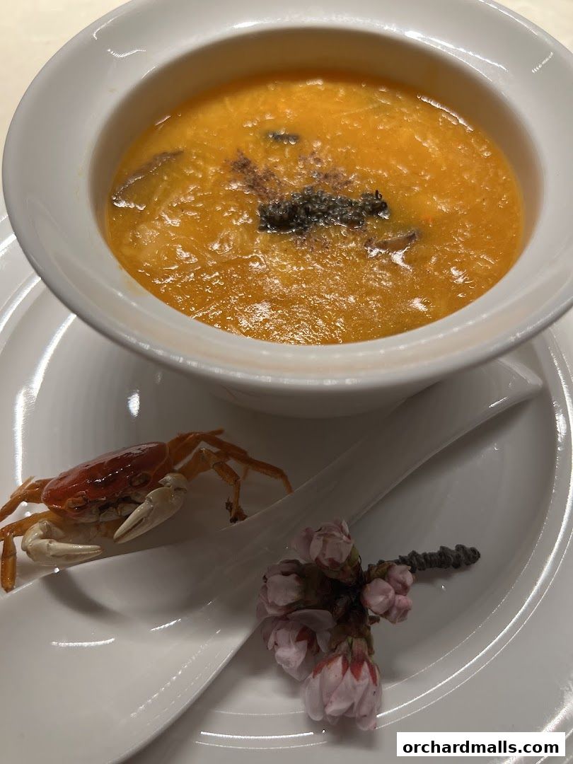 A bowl of orange soup with a crab and cherry blossoms on a spoon.