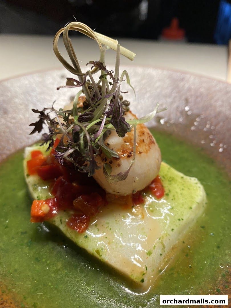 A beautifully plated dish featuring seared scallops atop a white fish fillet with a vibrant green sauce.