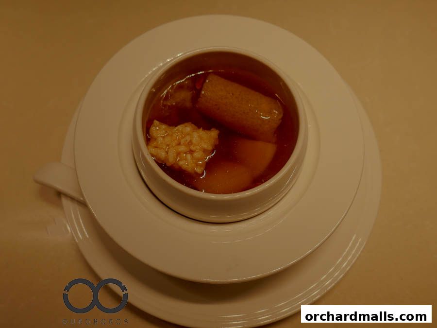 A close-up of a bowl of soup with ingredients and a logo at the bottom.