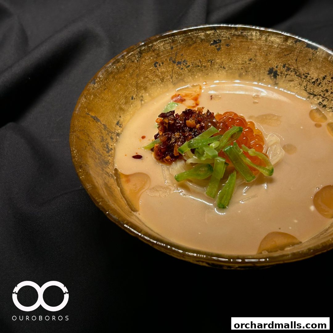 A close-up of a golden bowl filled with creamy soup, topped with chili, scallions, and roe.