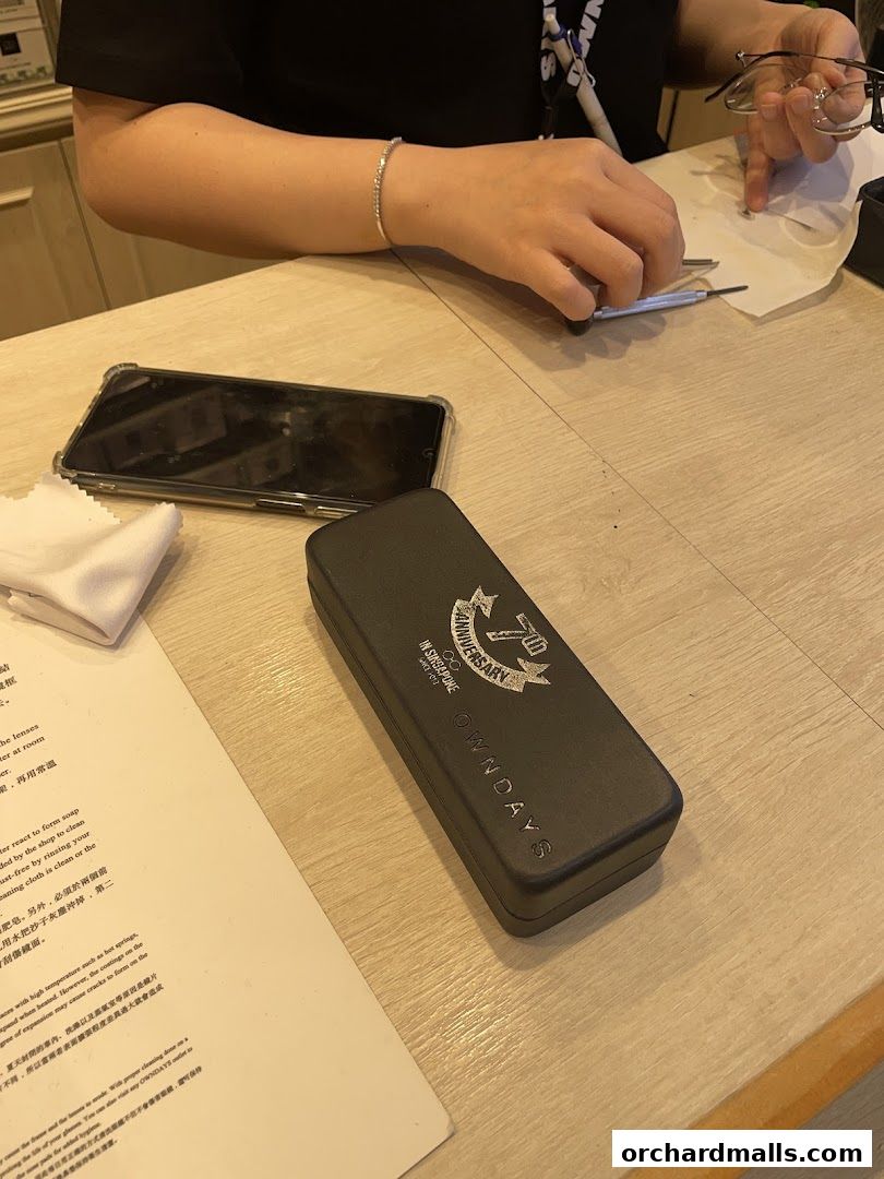 A close-up of a table with a phone, glasses case, and cleaning cloth.