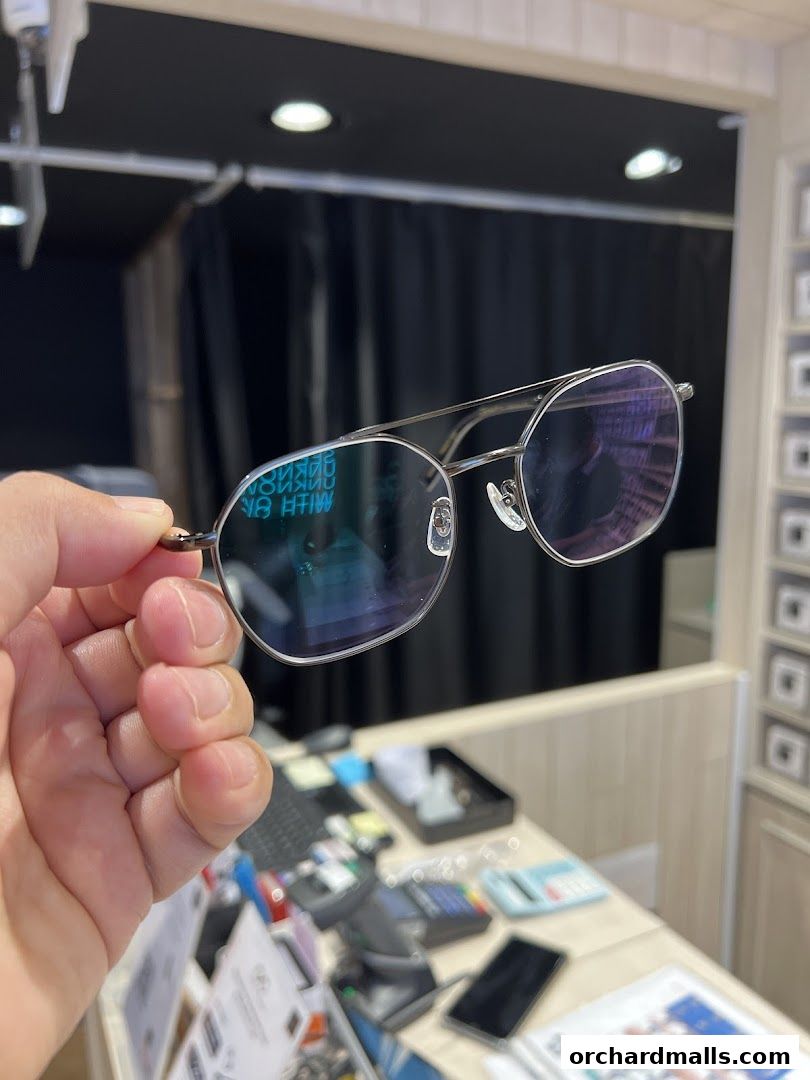 A hand holds up a pair of stylish aviator-style eyeglasses with blue-tinted lenses.