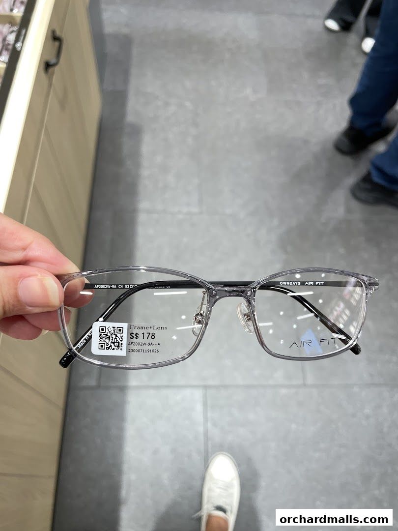A person holds up a pair of clear-rimmed glasses with the brand name OWNDAYS visible.