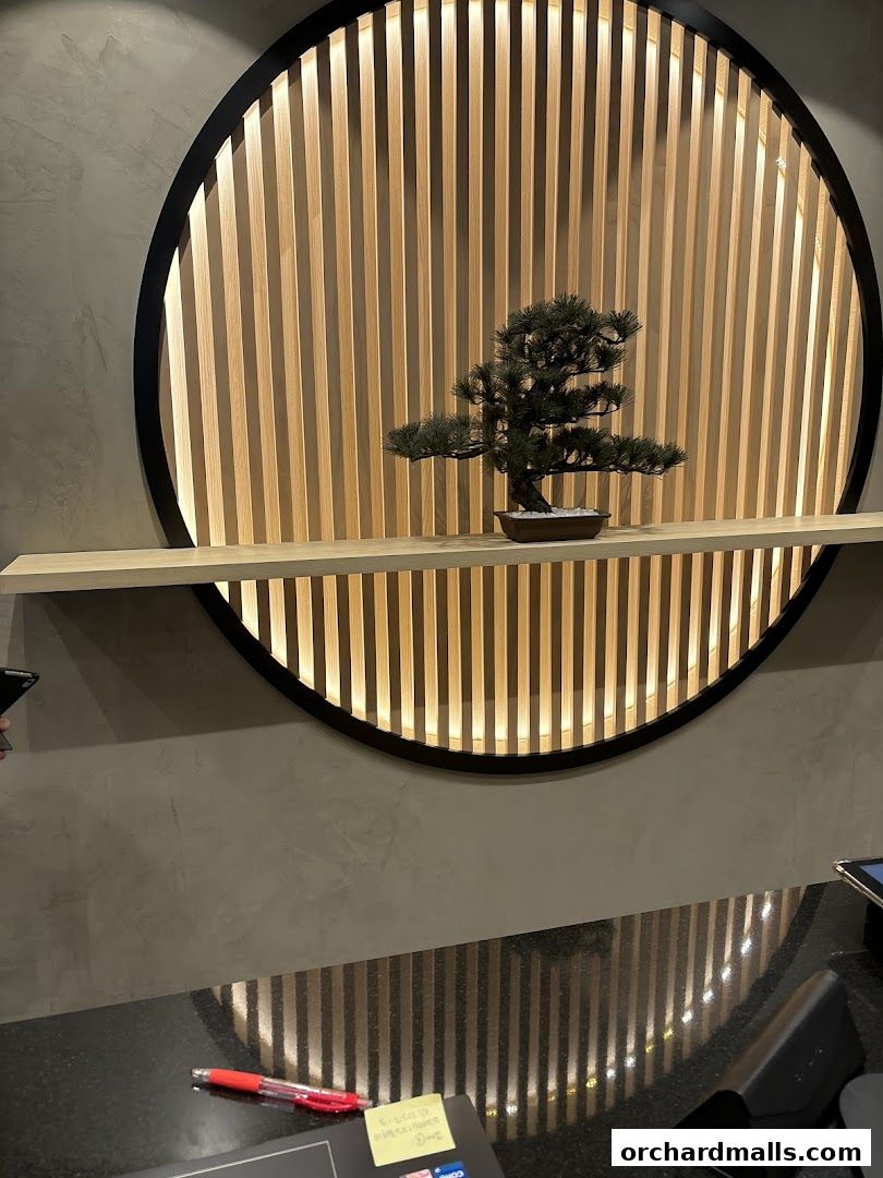 A decorative bonsai tree sits on a shelf in front of a backlit wooden slatted circle.