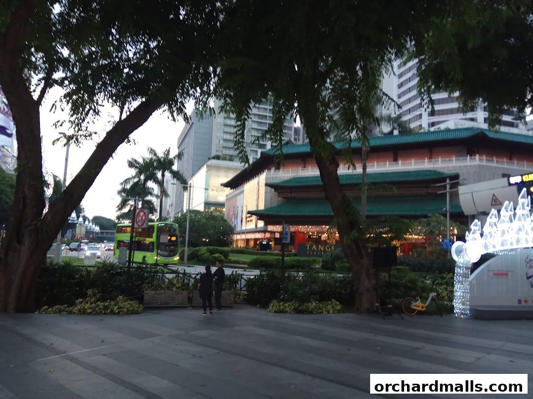 A street view of ION Orchard mall with a green double-decker bus and festive lights.