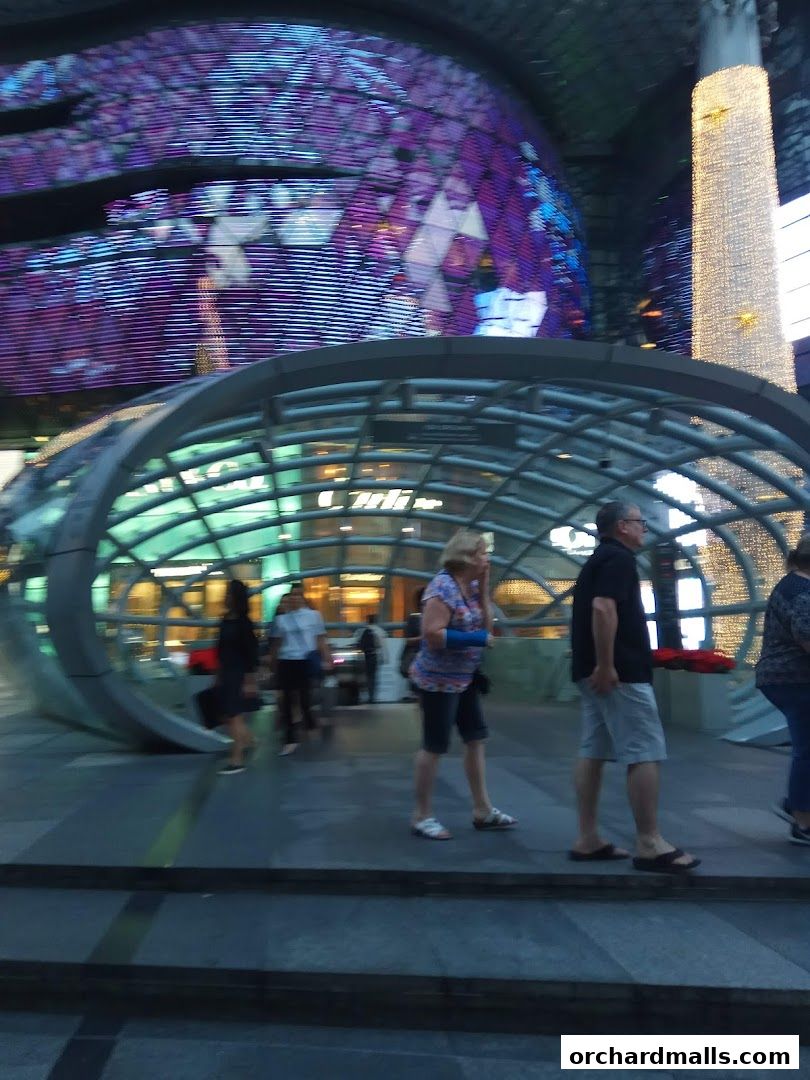 People walking past a modern architectural entrance with illuminated displays.