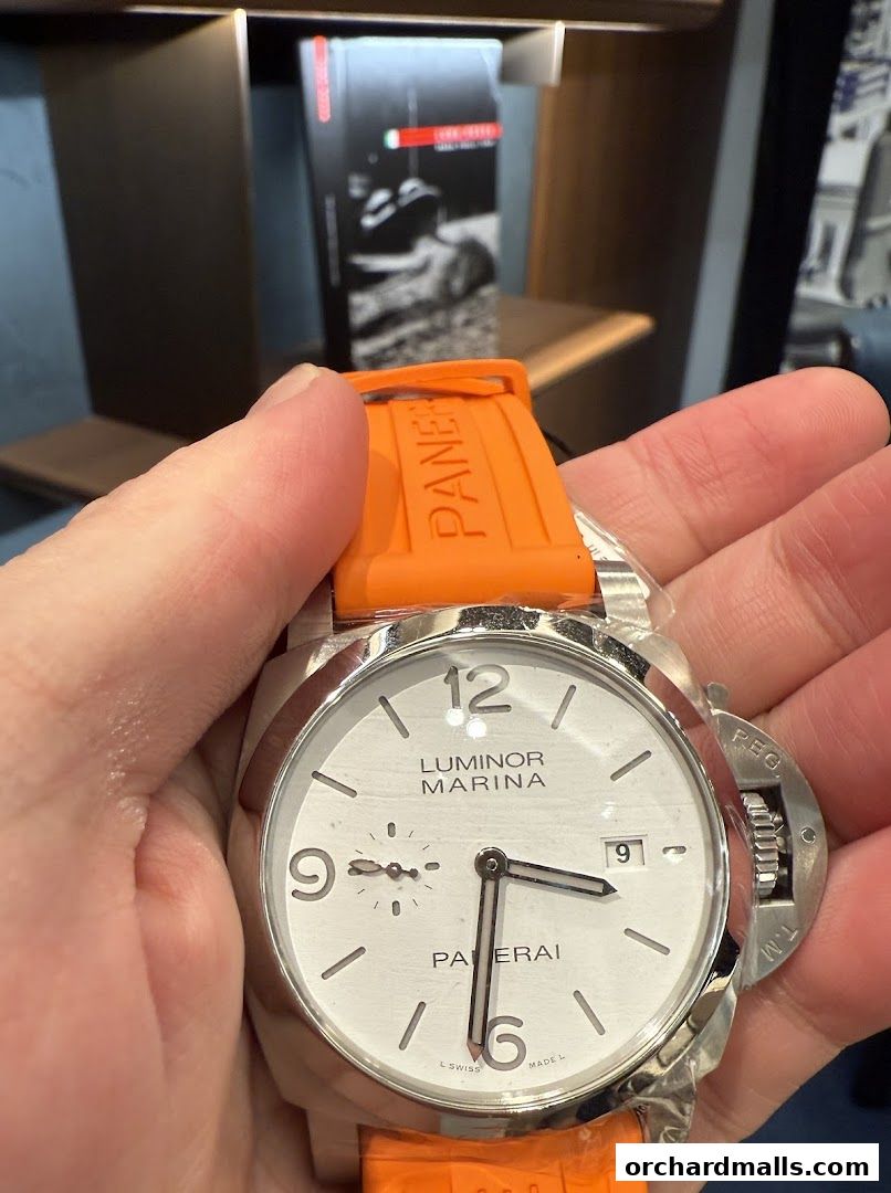 A hand holds a Panerai Luminor Marina watch with an orange strap.