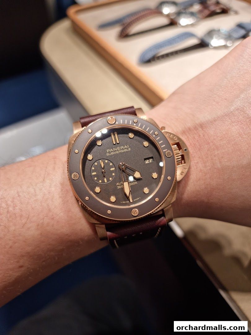 A close-up shot of a Panerai Submersible watch on a wrist, with watch straps in the background.