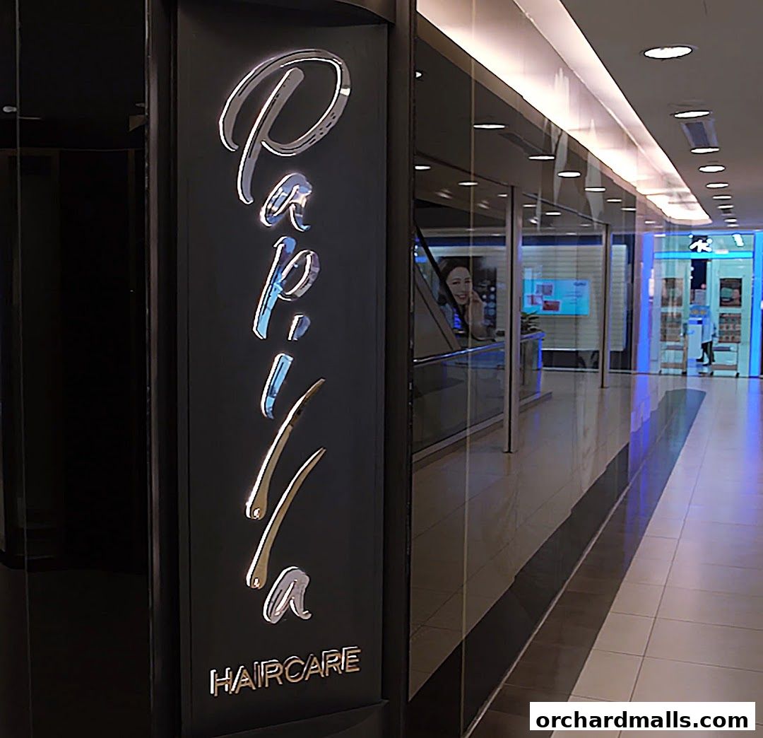 The illuminated sign for Papilla By Kim Lim Haircare in a modern shopping mall.