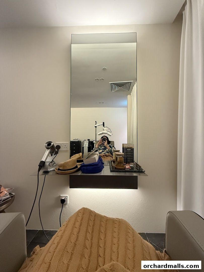 A salon chair with a blanket, hairdryer, hat, and mirror reflecting a person.