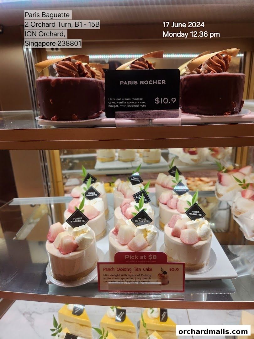 A display of beautifully crafted cakes at Paris Baguette, featuring 'Paris Rocher' and 'Peach Oolong Tea Cake'.