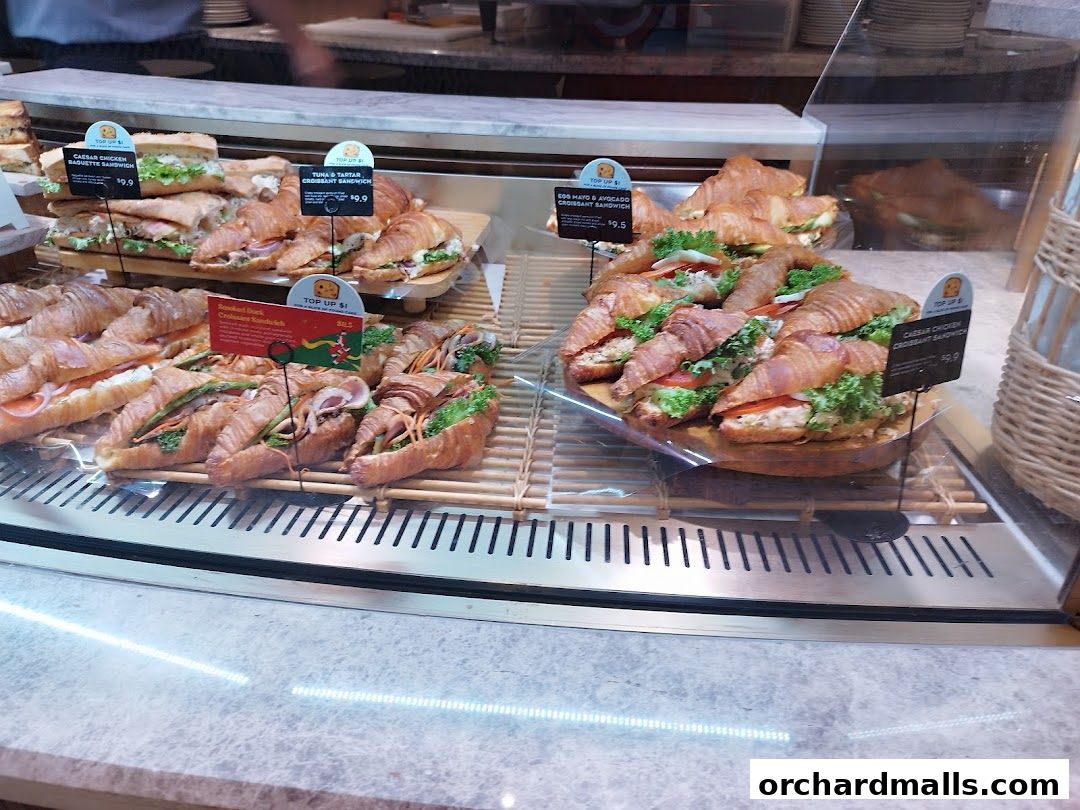 A display case filled with various croissants and sandwiches at Paris Baguette.