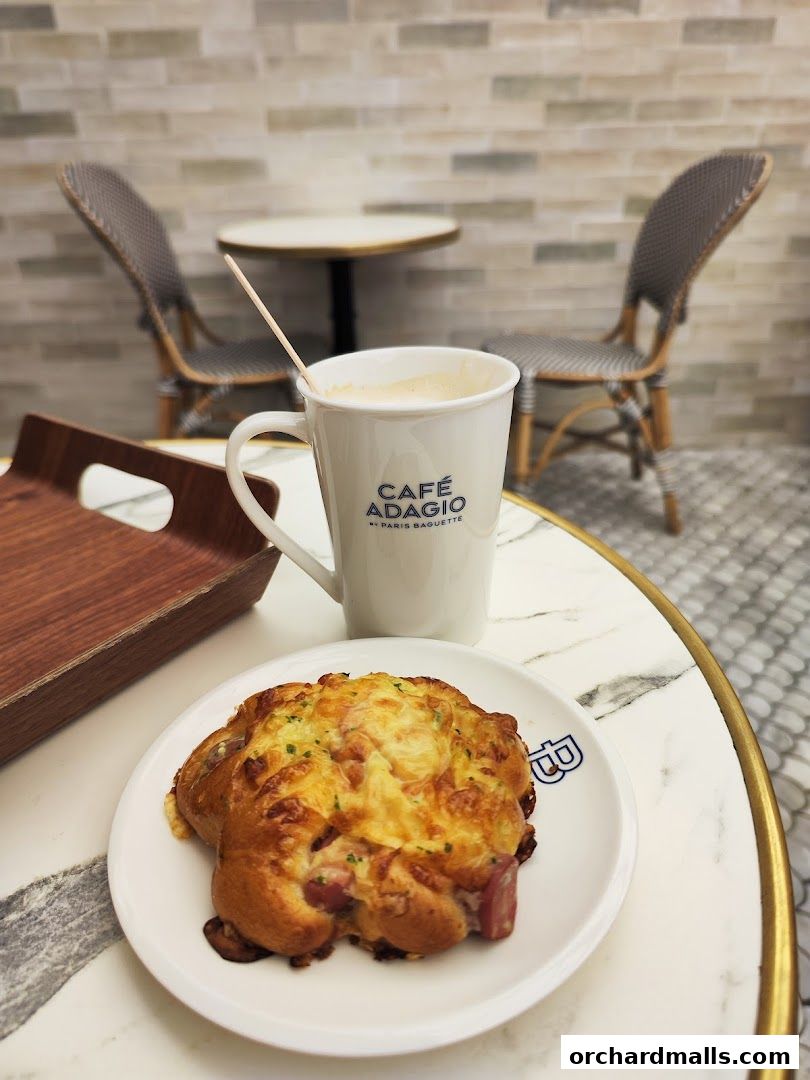 A savory pastry and a cup of coffee are displayed on a marble table with chairs in the background.