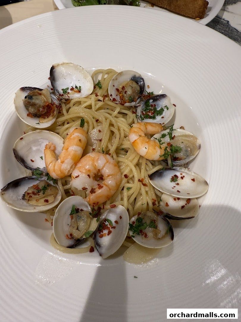 A close-up of a delicious seafood pasta dish with clams and shrimp, garnished with herbs and chili flakes.