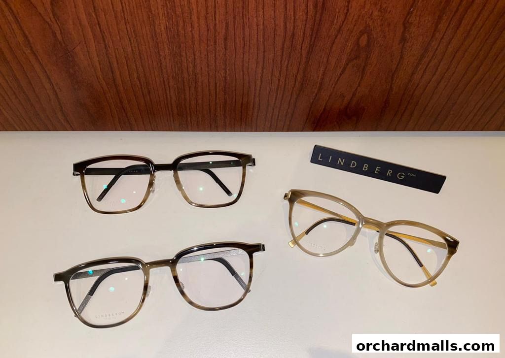 Three pairs of stylish eyeglasses and a LINDBERG brand sign are displayed on a white surface.