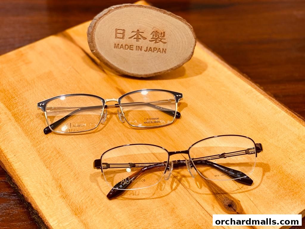 Two pairs of stylish eyeglasses displayed on a wooden surface with a 'Made in Japan' sign.