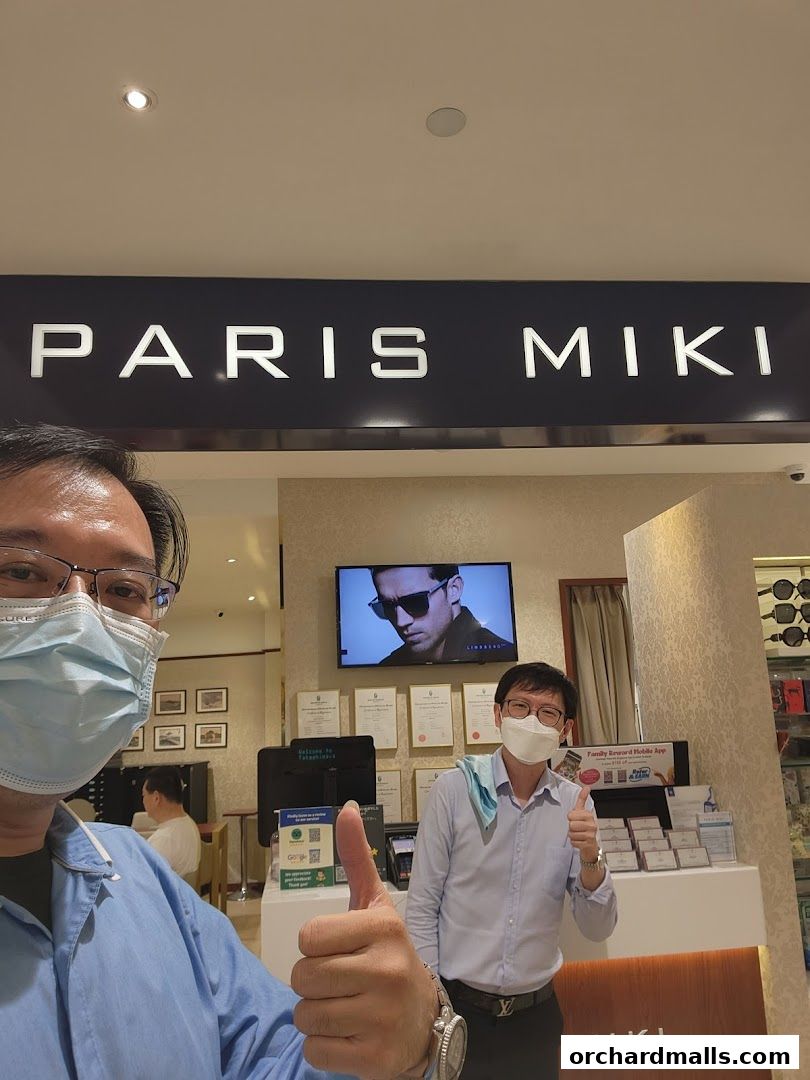 Two men give thumbs up in front of a Paris Miki optical shop.