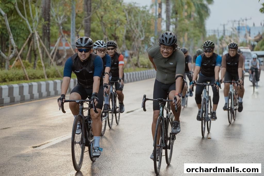 A group of cyclists wearing helmets and cycling gear ride on a wet road.