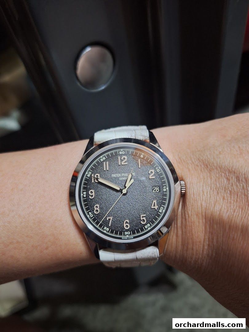A close-up shot of a Patek Philippe watch with a textured dark dial and a white leather strap on a wrist.