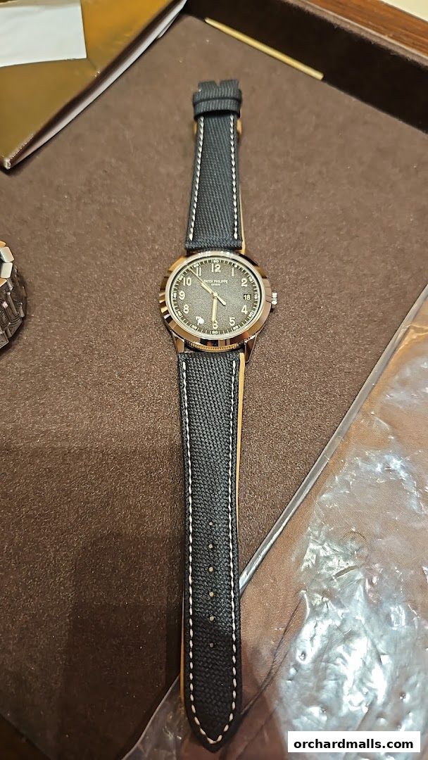 A close-up of a Patek Philippe watch with a dark textured dial and a black fabric strap.