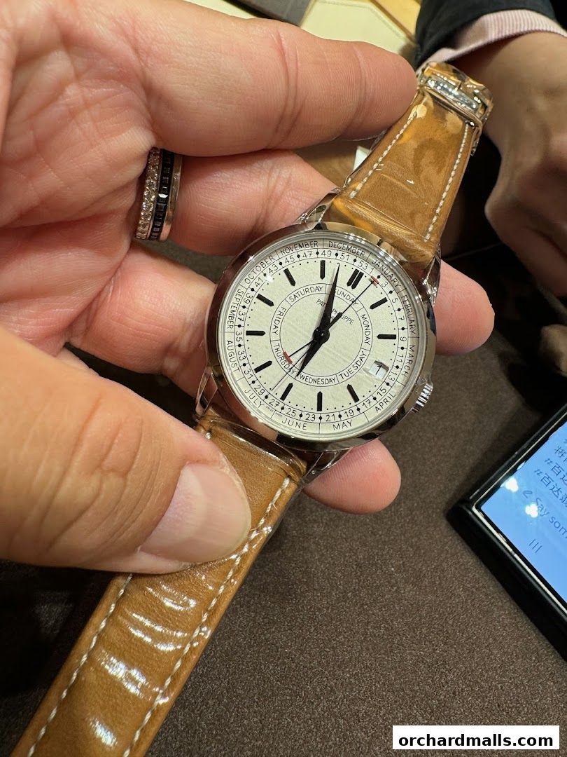 A person holds a Patek Philippe watch with a white dial and a brown leather strap.