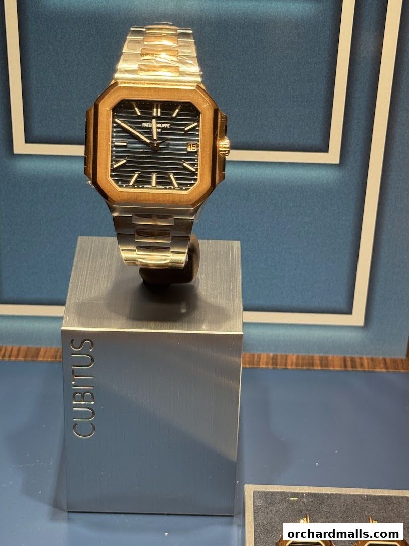 A Patek Philippe watch with a gold bezel and blue dial displayed on a stand.