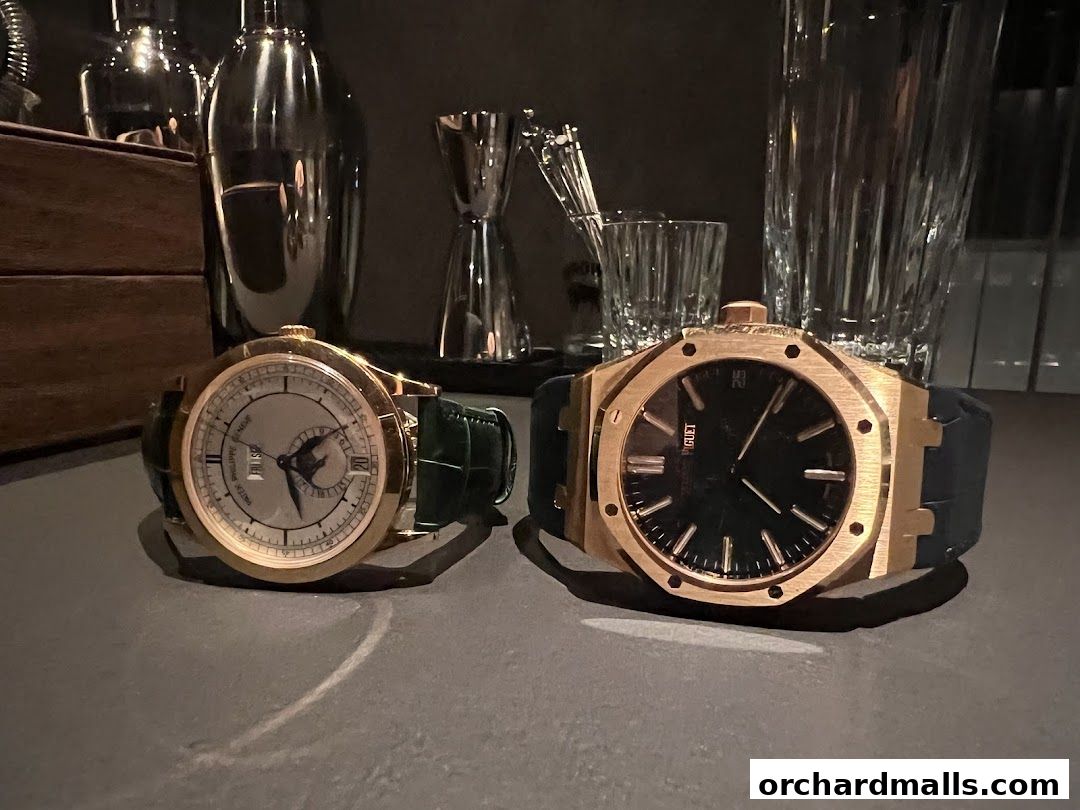 Two luxury watches, one Patek Philippe and one Audemars Piguet, displayed with barware.