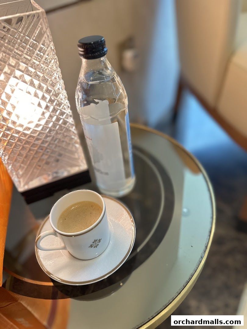 A cup of coffee and a bottle of water on a glass table with a lamp.