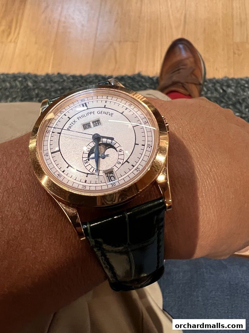 A close-up of a Patek Philippe watch with a rose gold case and a green alligator strap.