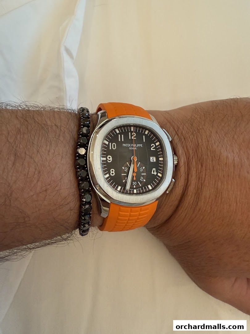 A close-up of a Patek Philippe watch with an orange strap and a diamond bracelet.