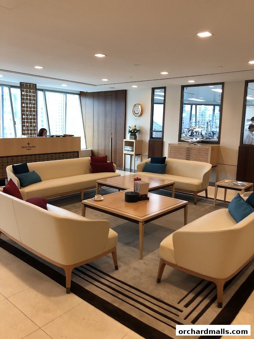 Luxurious waiting area with cream sofas, wooden tables, and a Patek Philippe reception desk.