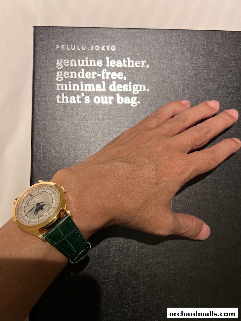 A hand wearing a Patek Philippe watch rests on a black box with brand messaging.