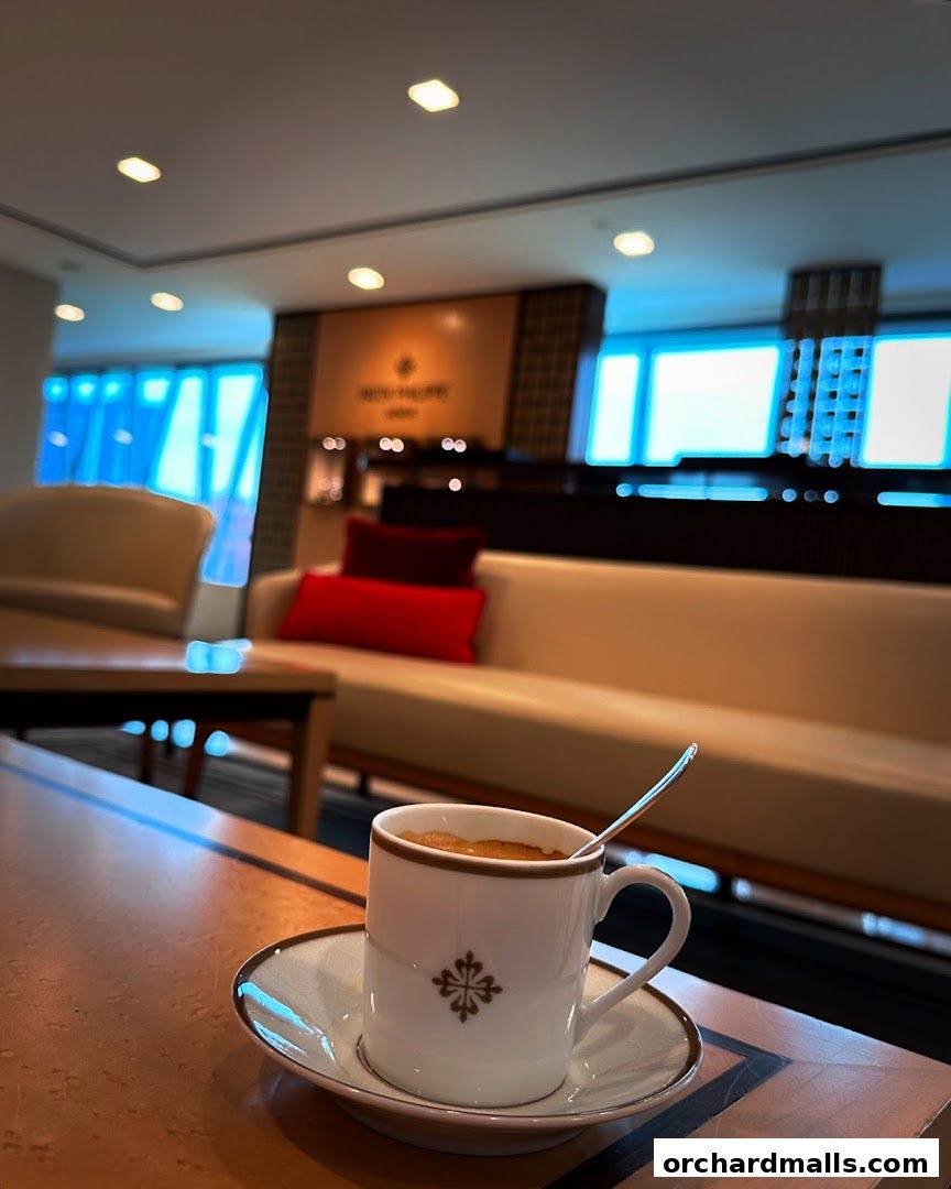 A cup of coffee sits on a table in a luxurious lounge area with Patek Philippe branding.