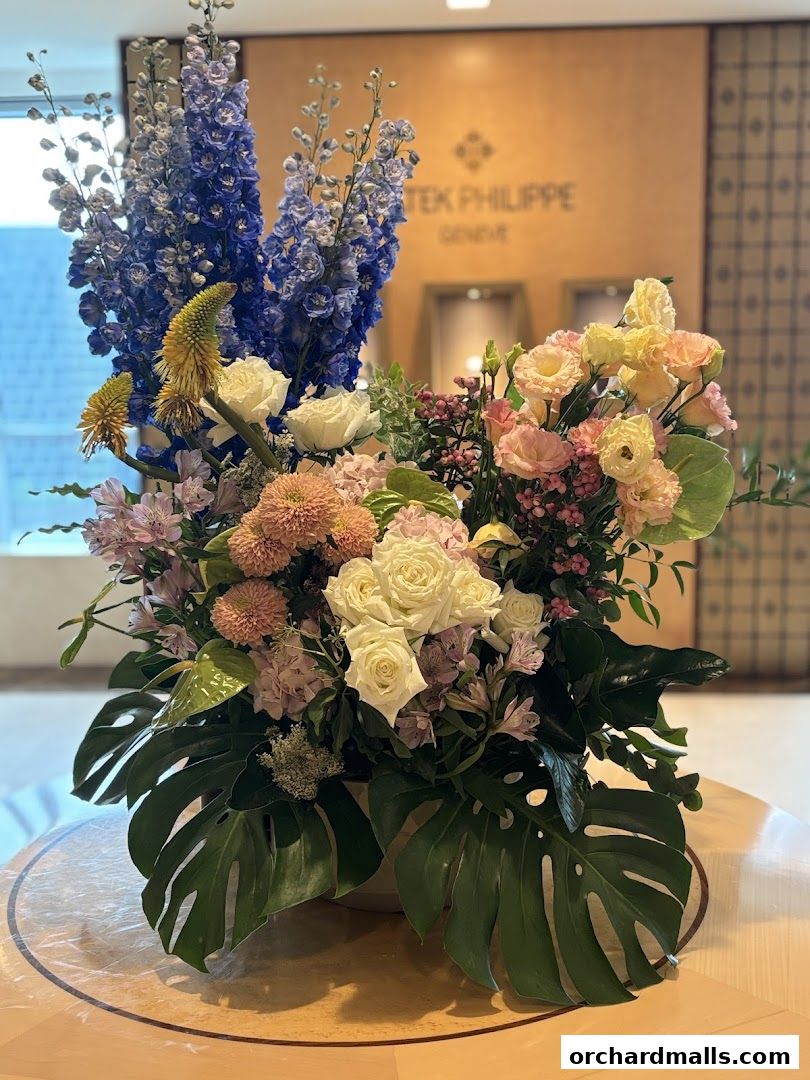 A large floral arrangement with blue delphiniums and roses in front of a Patek Philippe sign.