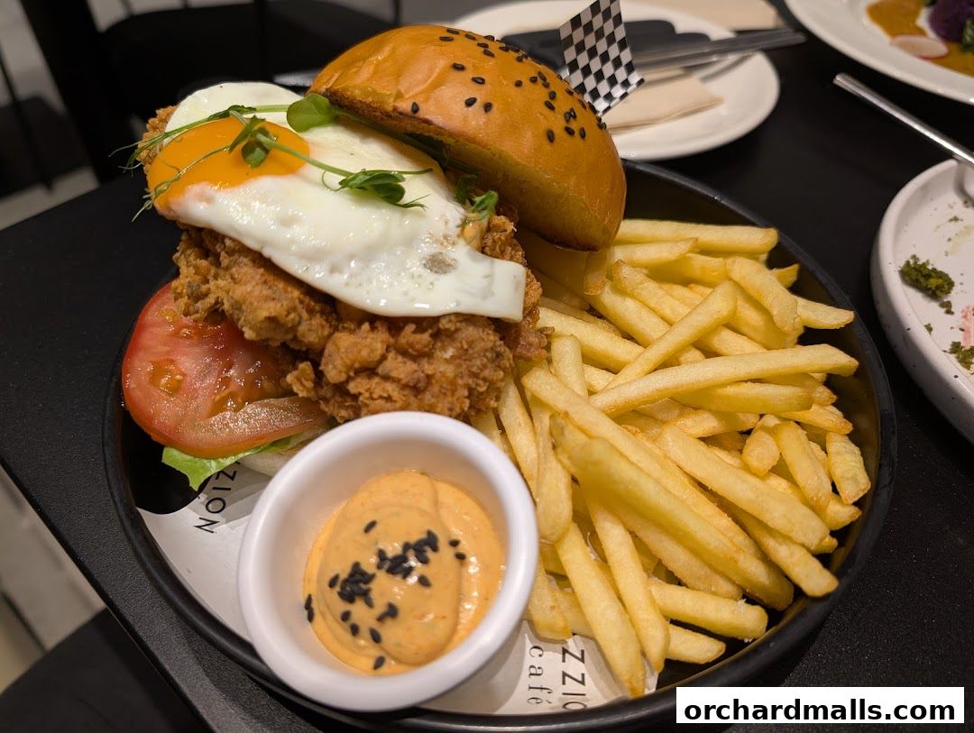 A delicious fried chicken burger with a sunny-side-up egg and fries, served at Pazzion Cafe.
