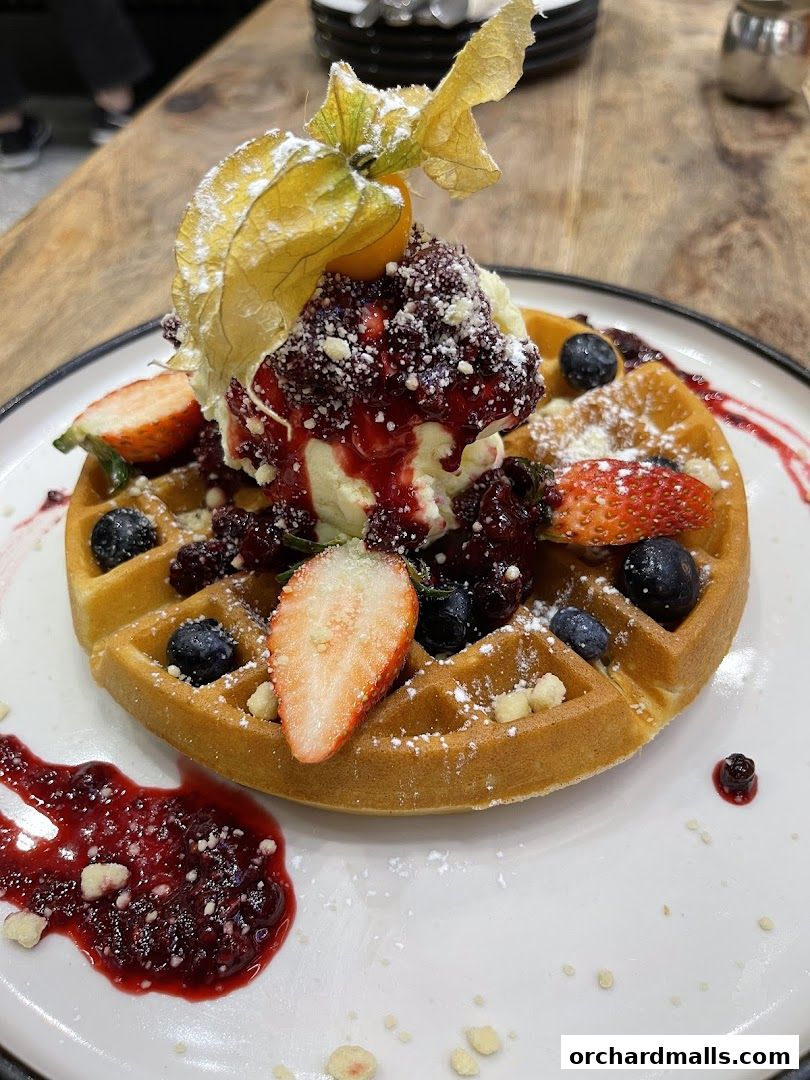 A delicious waffle topped with ice cream, berries, and a physalis.
