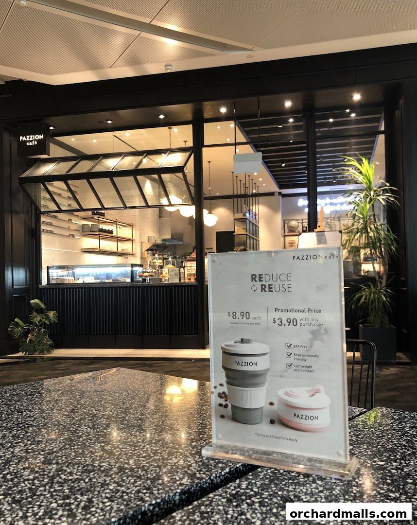 A sign promoting reusable cups is placed on a table in front of the Pazzion Cafe storefront.